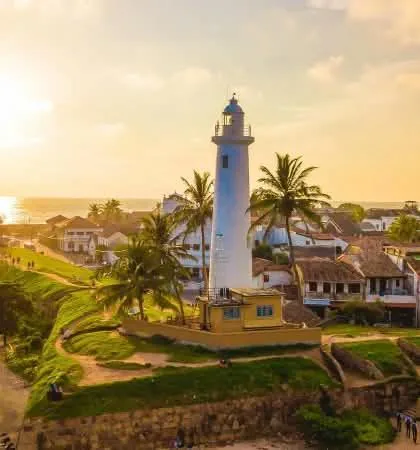 Galle lighthouse among palm trees at golden hour