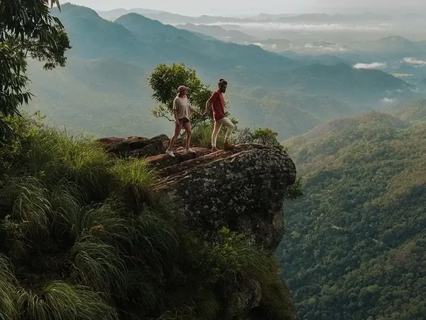 Two hikers on a cliff edge above misty hill-country valleys
